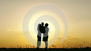 Silhouette of a happy family against a beautiful sunset. Father and mother hug and kiss their child. Emotions, kinship