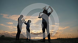 Silhouette of a happy family in the evening in the park. Mom plays with her son and touches his palms. The father is