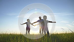 Silhouette of a happy family. Mom, dad, and son run across the field at sunset with their arms spread wide like wings