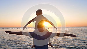 Silhouette of a happy family at sunset. A small boy sits on his father`s shoulders, swaying and imagining the flight of an airplan