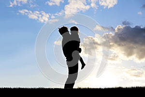 Silhouette of Happy Father Lovingly Hugging Little Child Outside at Sunset