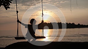 Silhouette of happy girl swaying on rope swings near amazing beach of paradise island at sunset. Slow motion