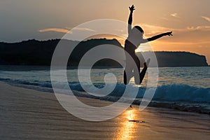 Silhouette of happy joyful woman jumping and having fun at the beach against the sunset. Freedom and leisure vacation concept.