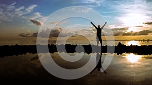 Silhouette of a happy man standing on the beach with his arms wide open showing victory during sunrise morning with reflection. photo