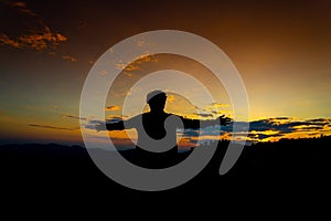Silhouette Happy Man Standing on Hill at the Sunset on Mountain with Orange Sky. Enjoying Peaceful Moment Concept. Relaxing or