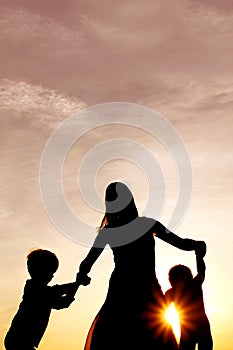Silhouette of happy mother and little children dancing outside a