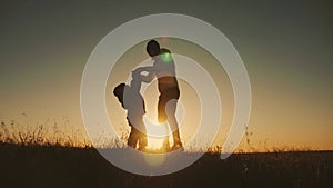 Silhouette happy mother and little son are playing around while walking outside at sunset.