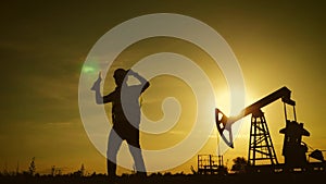 Silhouette of happy oilfield worker at crude oil pump in the oilfield at golden sunset. Industry, oilfield, people and