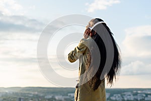 Silhouette of happy smiling young black african american woman with long hair listening to music. Blurred cityscape on