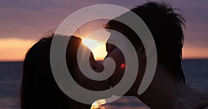 Silhouette of happy teenage couple girl kissing boyfriend on the sandy beach behind the sunset after romantic evening date