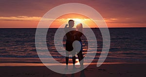 Silhouette of happy teenage couple girl kissing boyfriend on the sandy beach behind the sunset after romantic evening date