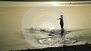 Silhouette of a happy teenage girl running into a pond at sunset