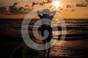 Silhouette of Happy woman standing with hands on head while sunset at sea,Freedom concept,Light flare
