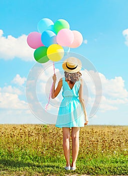 Silhouette happy woman stands with an air colorful balloons in a straw hat enjoying a summer day on field and blue sky backgroun