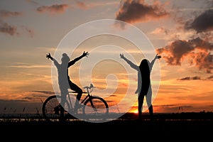 Silhouette of happy women with bicycle open hands