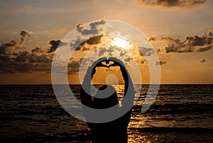 Silhouette of Happy woman showing fingers shape of heart on sunset at sea,Love is all around