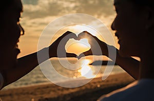 Silhouette of happy young couple forming a heart shape with their hands together on the beach while golden sunset time and sea