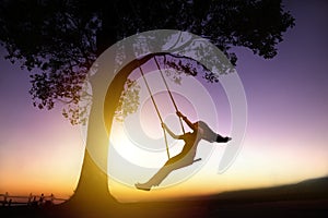 Silhouette of happy young woman on swing photo