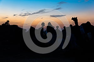 Silhouette head shot of camel and camel herders at sunset.