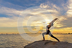 Silhouette healthy woman lifestyle exercising vital meditate and practicing yoga outdoors on the rock at beach sunset and twiligh