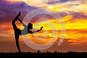 Silhouette of healthy woman practicing yoga meditation during on background city with sky and sunset
