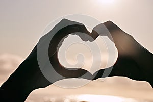 Silhouette, heart hands and couple at beach for sunset, love and bonding for care together on summer holiday. Shadow