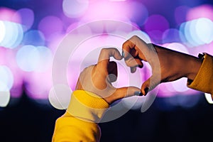 Silhouette of a heart shaped hands and crowd of Audience at live concert, light illuminated is power of music concert