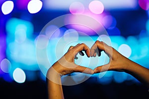 Silhouette of a heart shaped hands and crowd of Audience at live concert, light illuminated is power of music concert