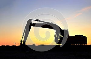 Silhouette of the heavy tracked excavator at a construction site on a background sunset.
