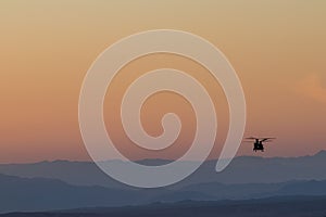 Silhouette of helicopter in orange sunset sky with silhouettes of mountains