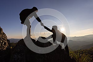Silhouette of helping hand between two climber.  couple hiking help each other silhouette in mountains with sunlight. The men