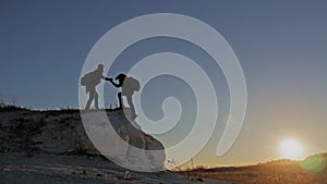 Silhouette of helping hand between two climber. two hikers on top of the mountain, a man helps a man to climb a sheer