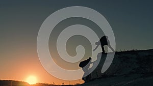 Silhouette of helping hand between two climber. two hikers on top of the mountain, a man helps a man to climb a sheer