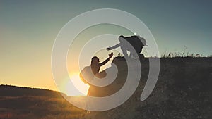 Silhouette of helping hand between two climber. two hikers on top of the mountain, a man helps a man to climb a sheer