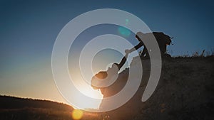 Silhouette of helping hand between two climber. two hikers on top of the mountain, a man helps a man to climb a sheer