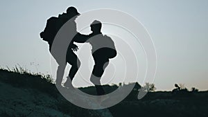 Silhouette of helping hand between two climber. two hikers on top of the mountain, a man helps a man to climb a sheer