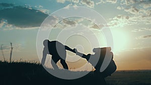 Silhouette of helping hand between two climber. two hikers on top of the mountain, a man helps a man to climb a sheer