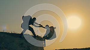 Silhouette of helping hand between two climber. two hikers on top of the mountain, a man helps a man to climb a sheer