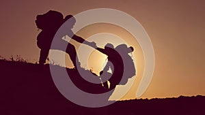 Silhouette of helping hand between two climber. two hikers on top of the mountain, a man helps a man to climb a sheer