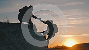 Silhouette of helping hand between two climber. two hikers on top of the mountain, a man helps a woman to climb a sheer