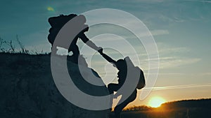 Silhouette of helping hand between two climber. two hikers on top of the mountain, a man helps a woman to climb a sheer
