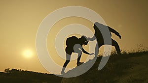 Silhouette of helping hand between two climber. two hikers on top of the mountain, a man helps a woman to climb a sheer