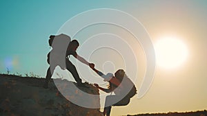 Silhouette of helping hand between two climber. two hikers on top of the mountain, a man helps a woman to climb a sheer