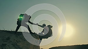 Silhouette of helping hand between two climber. two hikers on top of the mountain, a man helps a woman to climb a sheer