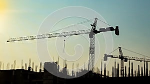 Silhouette of high construction site cranes at sunset