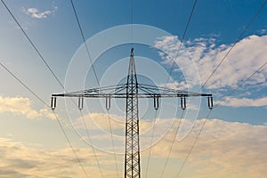 Silhouette of a high voltage mast at cloudy sky at sunset