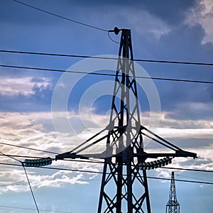 Silhouette of a high-voltage power line tower against cloudy sky in the evening