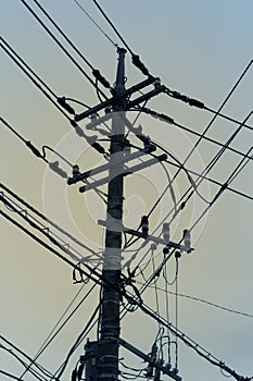 Silhouette of highly loaded urban electricity pole with many cables against orange sunset sky