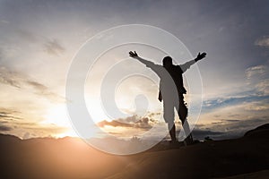 Silhouette of hiker standing on top of hill and enjoying sunrise over the valley.  The man thank God on the mountain