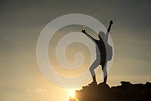 Silhouette hiker woman raise hands to celebrate after climbing to mountain summit at sunset. Extreme outdoor adventure sport